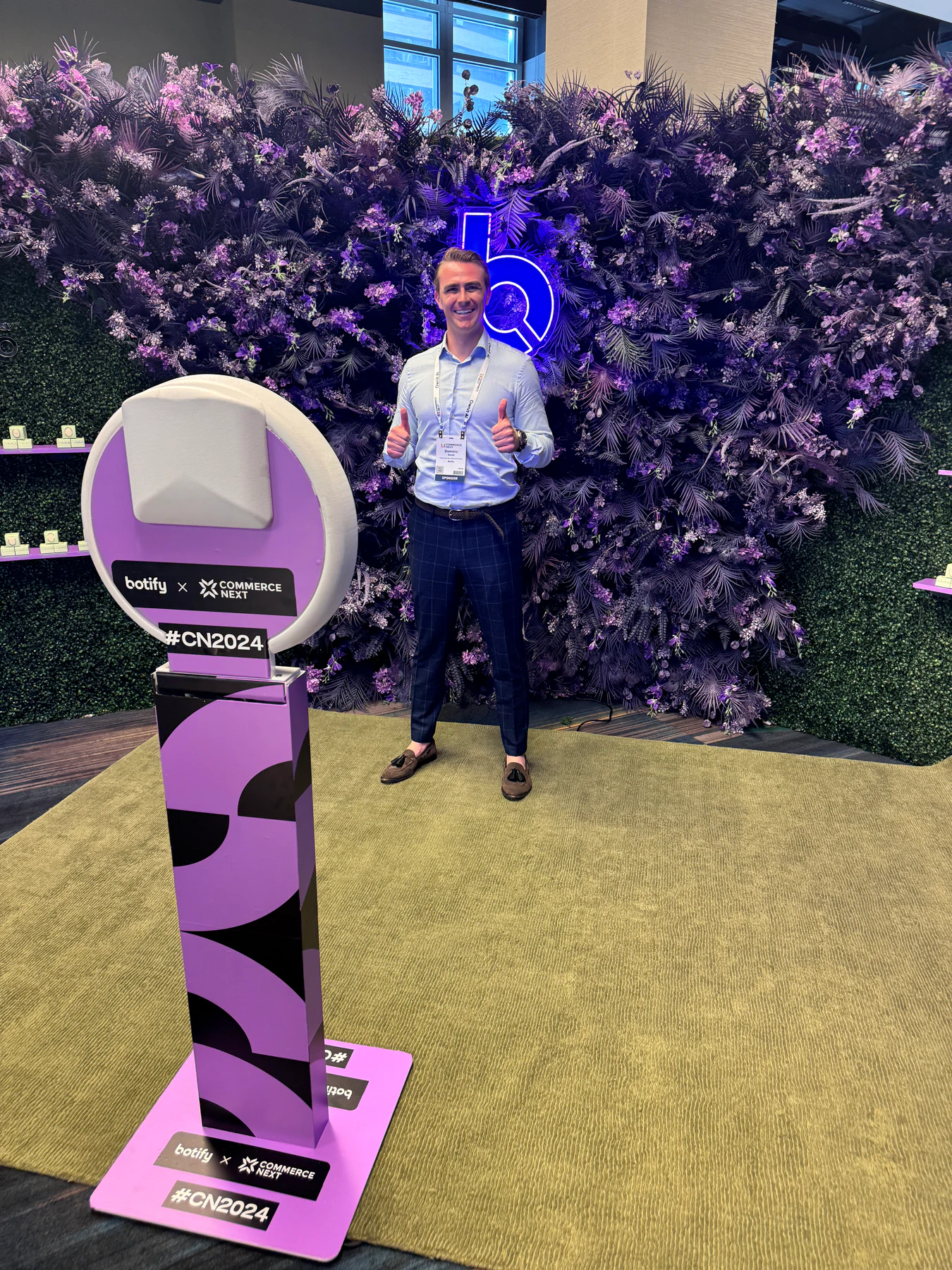 Branded photo booth in front of a purple floral wall with a neon logo at a corporate activation