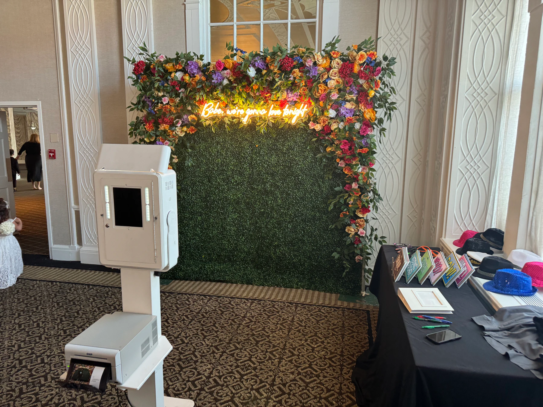 Photo booth beside a floral arch and greenery wall installed in a New York venue