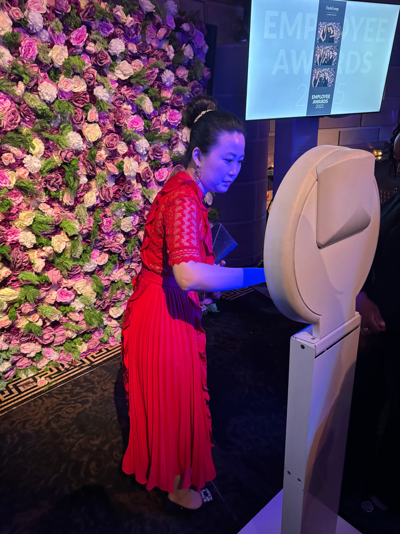 Guest using a photo booth beside a pink and lilac flower wall at a New York event