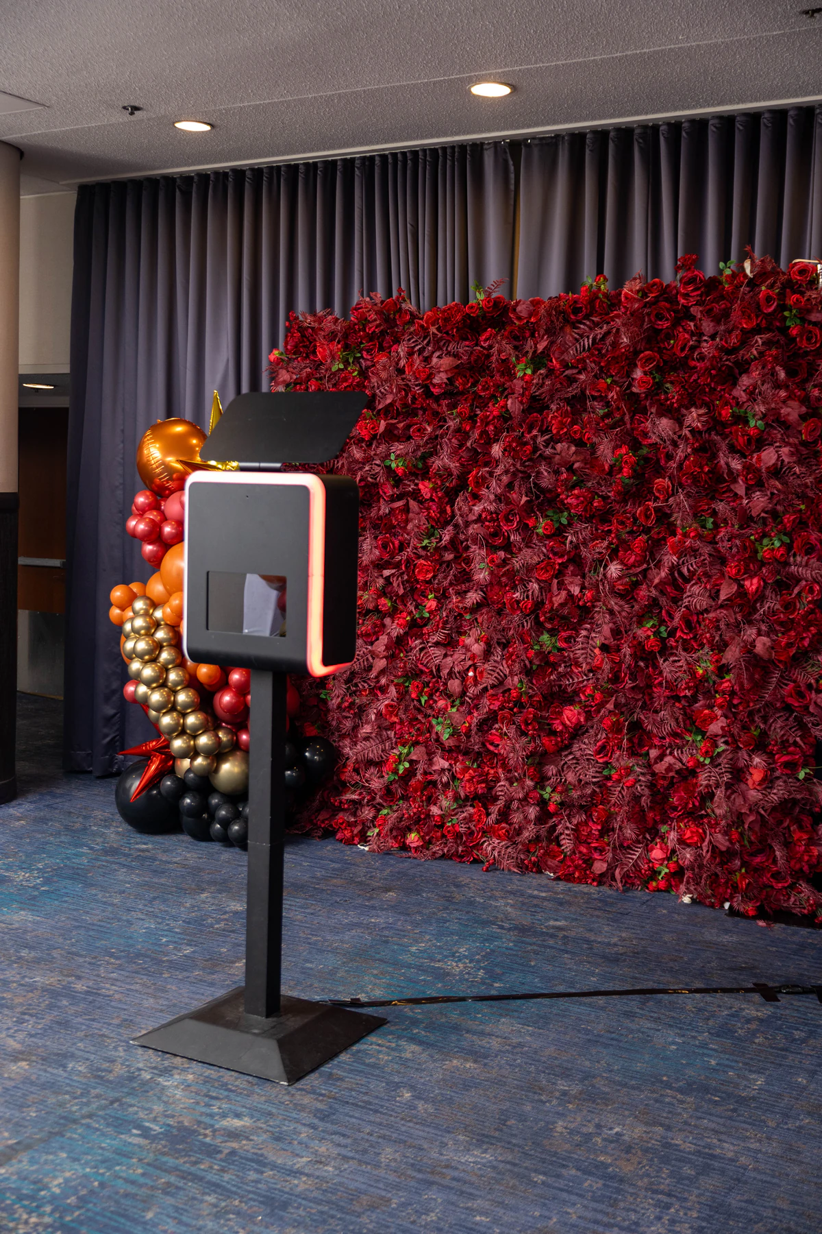Photo booth beside a deep red flower wall dressed with a balloon installation