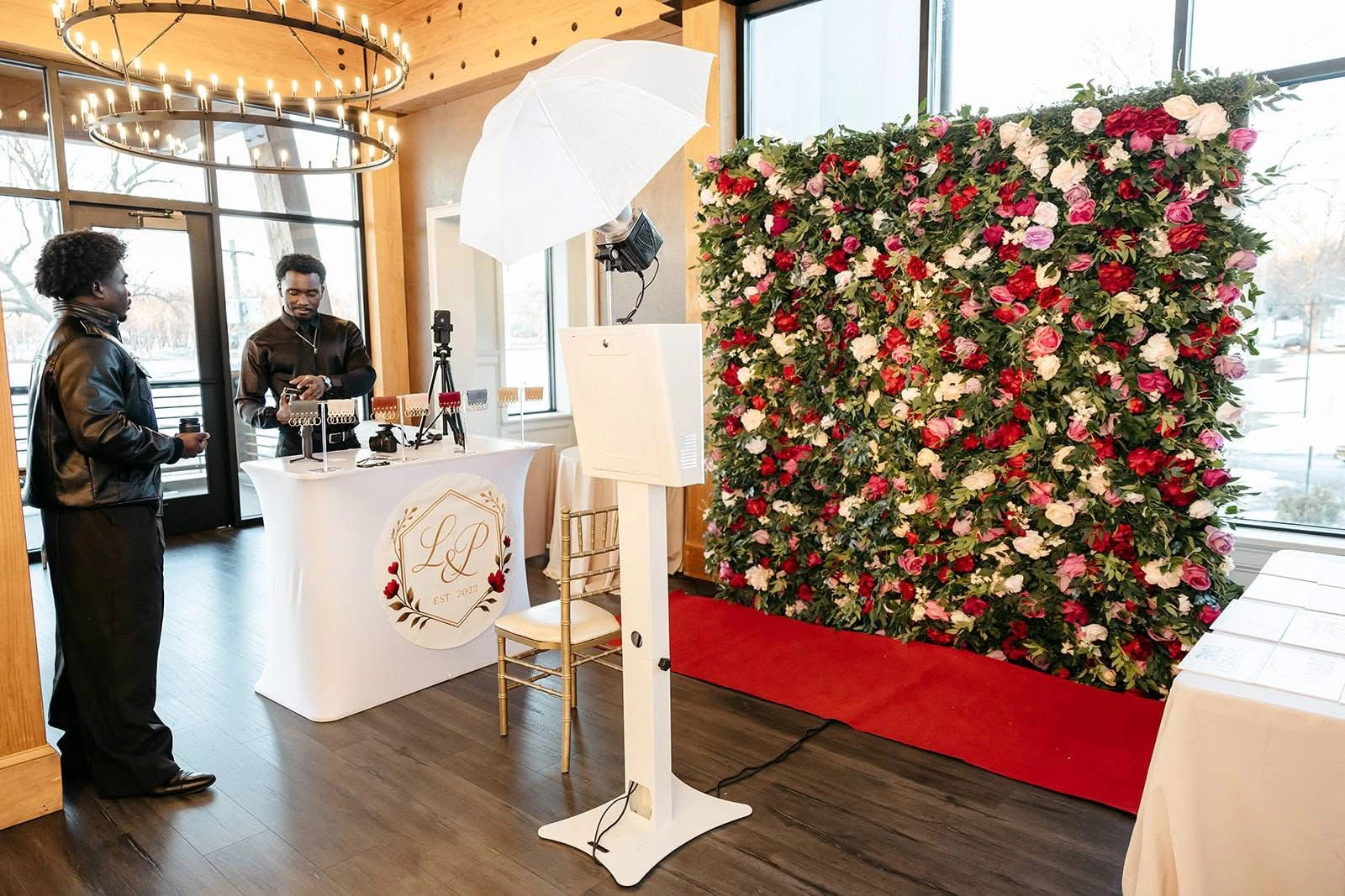 Photo booth set up beside a red and pink rose flower wall at a New York wedding, with the attendant preparing the booth
