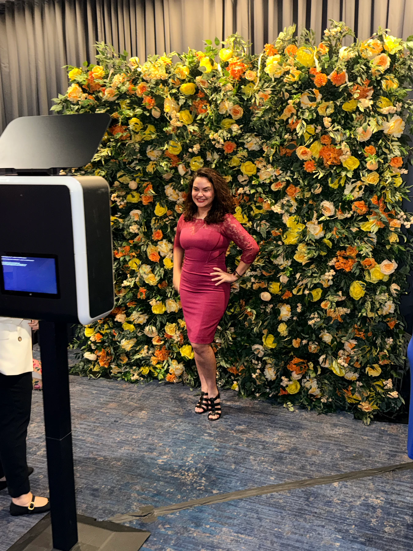 Guest beside a yellow and orange flower wall with a photo booth at a New York event