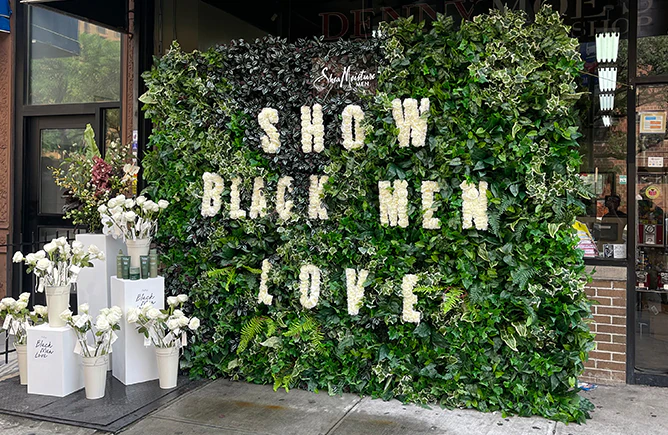Greenery wall with white floral lettering spelling a campaign message, installed outside a New York storefront