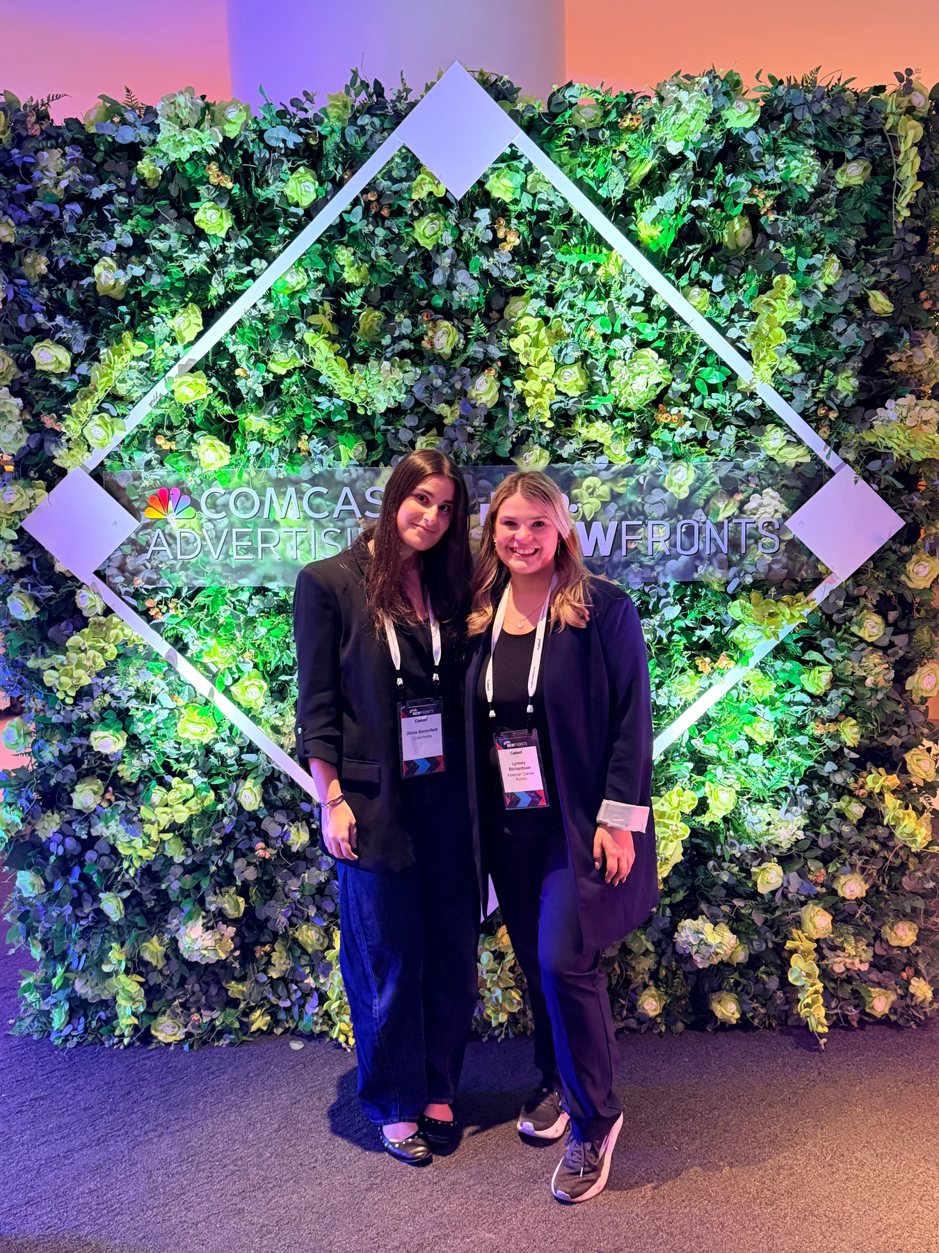 Attendees photographed at a Manhattan corporate event in front of a branded greenery wall