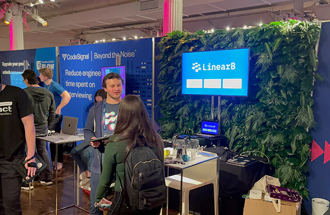 Attendees at a branded greenery wall on a New York trade show floor, with company signage set into the installation