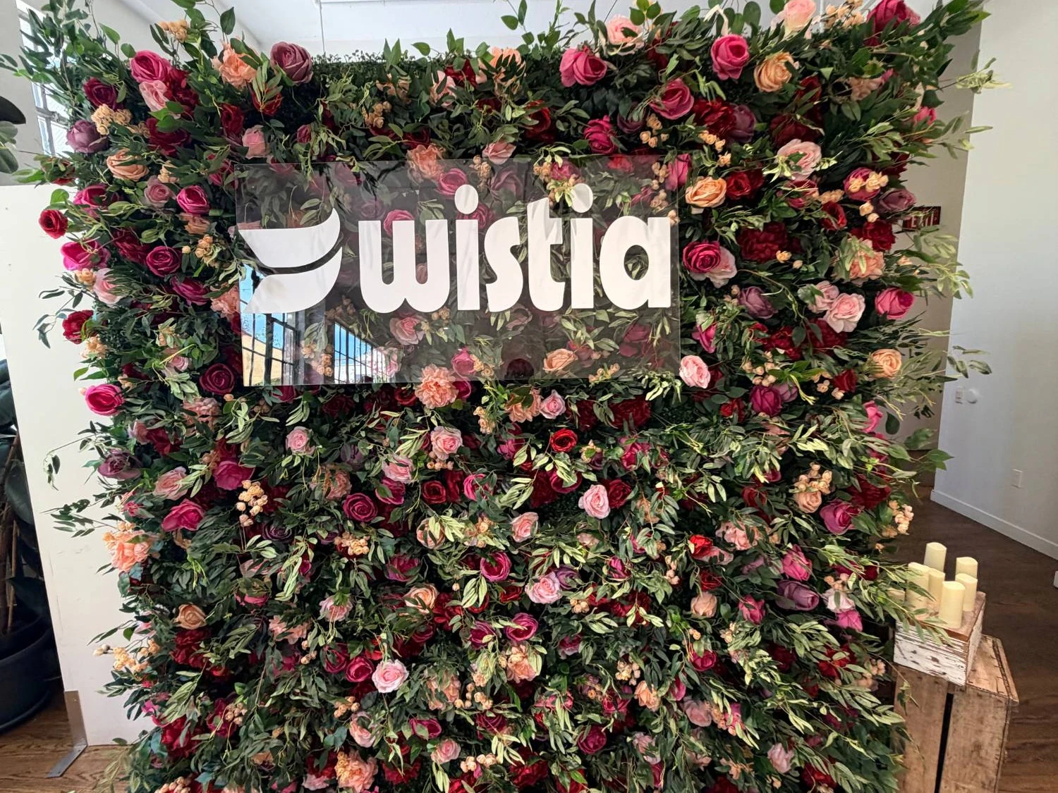 Deep red and pink rose wall with a brushed acrylic Wistia logo mounted across it at a corporate event