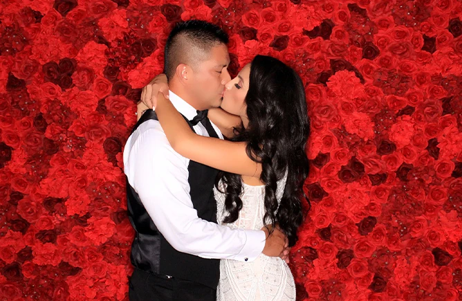 Couple photographed together in front of a red rose flower wall