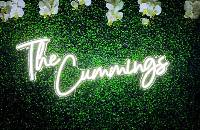 White neon family name sign on a greenery wall dressed with white orchids