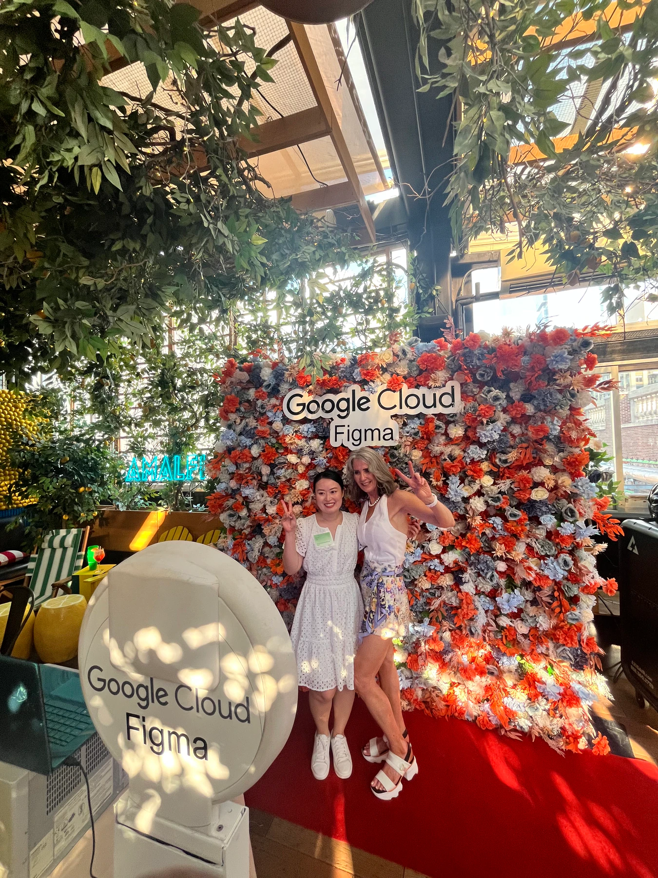 Two guests posing at a photo booth beside a branded flower wall at a Google Cloud and Figma event in New York