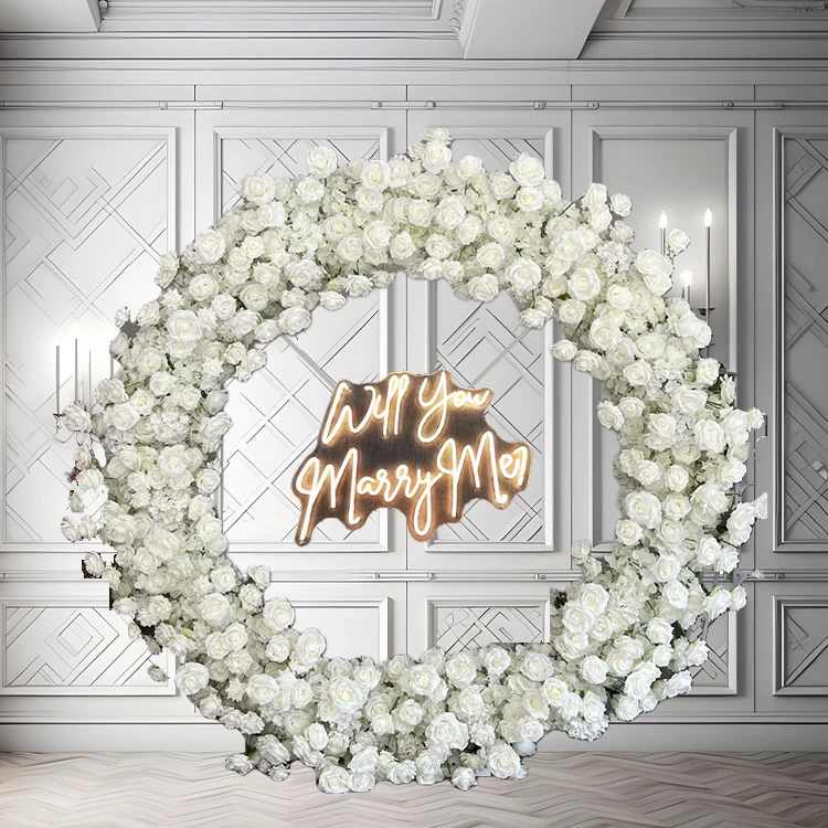 White circular floral arch with an illuminated Marry Me neon sign set inside it